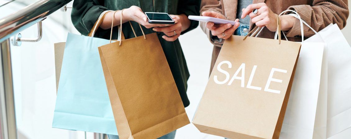 hands-of-two-young-contemporary-shoppers-with-smartphones-and-paperbags-scrolling-through-online-goods-and-comparing-prices hands-of-two-young-contemporary-shoppers-with-smartphones-and-paperbags-scrolling-through-online-goods-and-comparing-prices